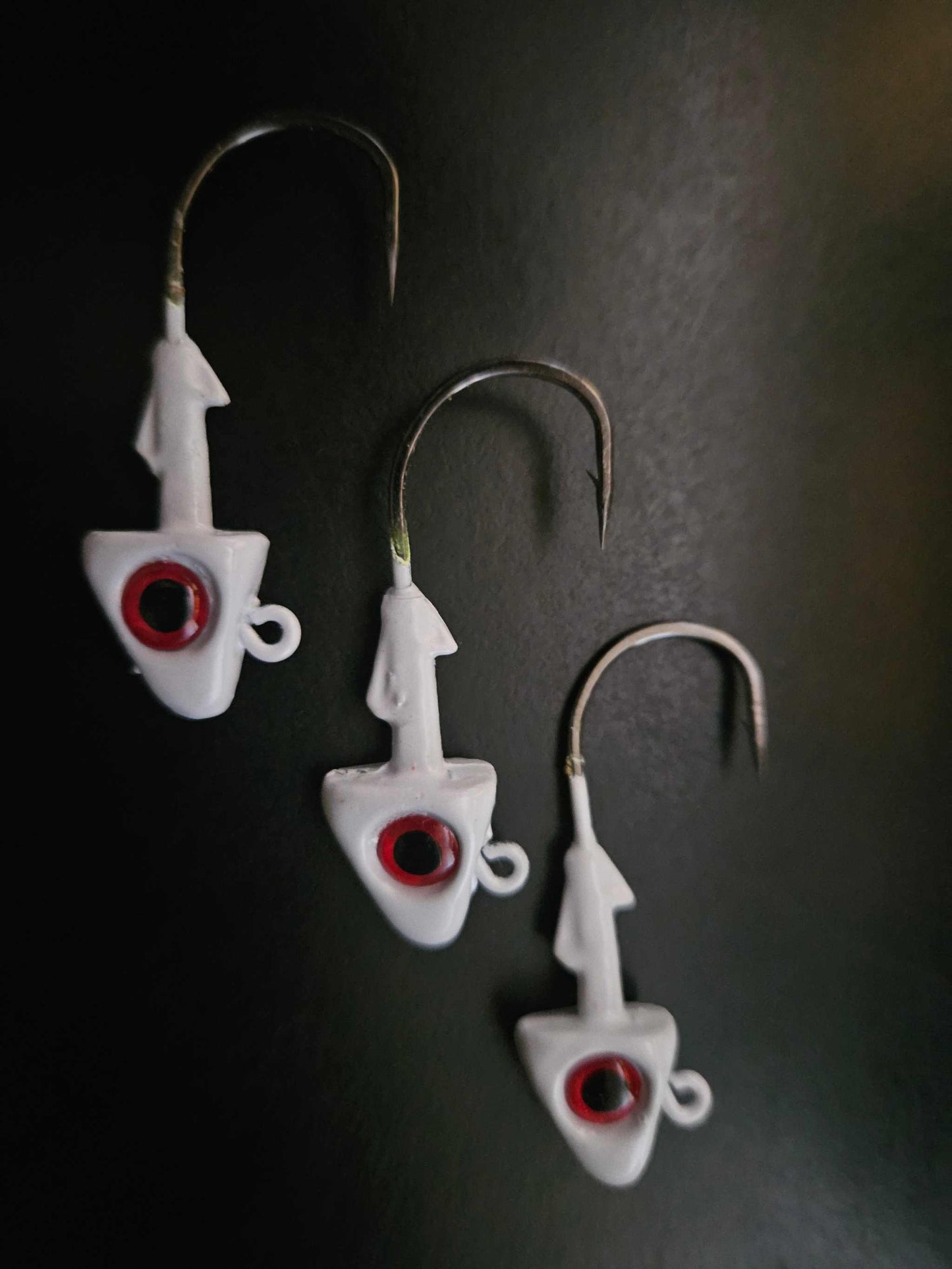 A picture showing 3 EZ Jig Heads, ½ oz, White with Red eyes and 3/0 Hooks on a black background.