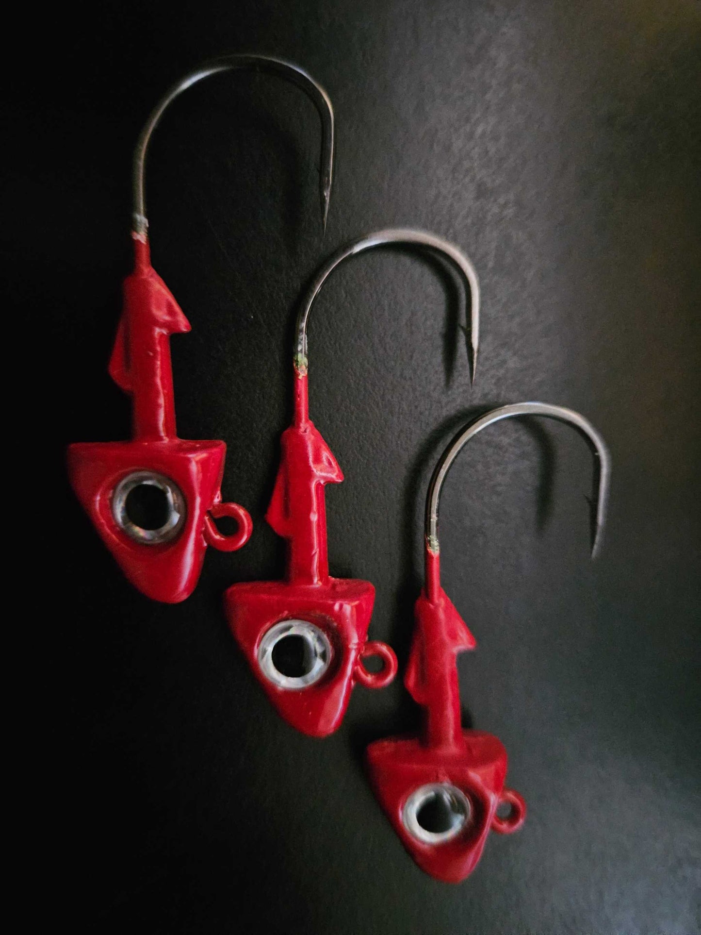 A picture showing 3 EZ Jig Heads, ½ oz, Red with Silver eyes and 3/0 Hooks on a black background.