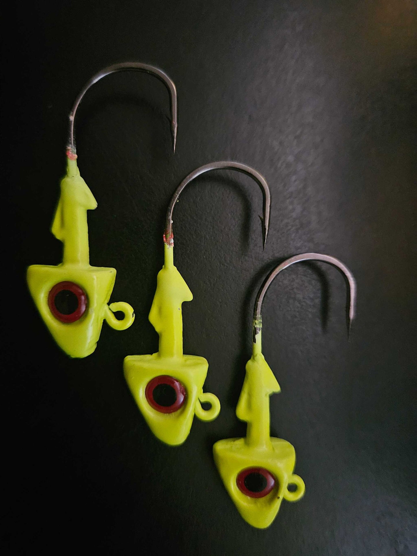 A picture showing 3 EZ Jig Heads, ½ oz, Yellow with red eyes and 3/0 Hooks on a black background.
