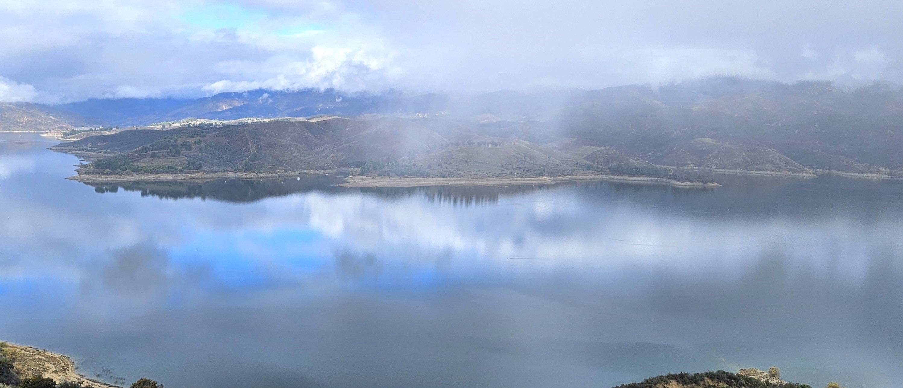 An image of a lake during scattered storms. More sky is visible in the reflection off of the lake than the in the sky.